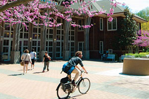 A student riding a bicycle in front of Dutton Hall