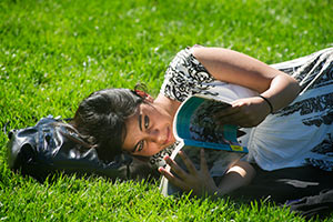 A female student laying on the grass of the quad, reading a book